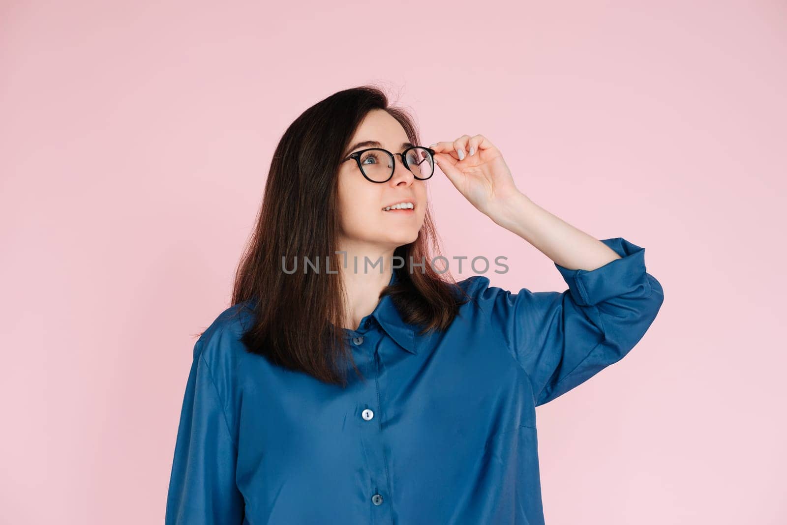 Thoughtful Woman in Glasses, Touching Her Frames, Deep in Contemplation, Searching for Ideas in Empty Space: Isolated Pink Background Portrait.