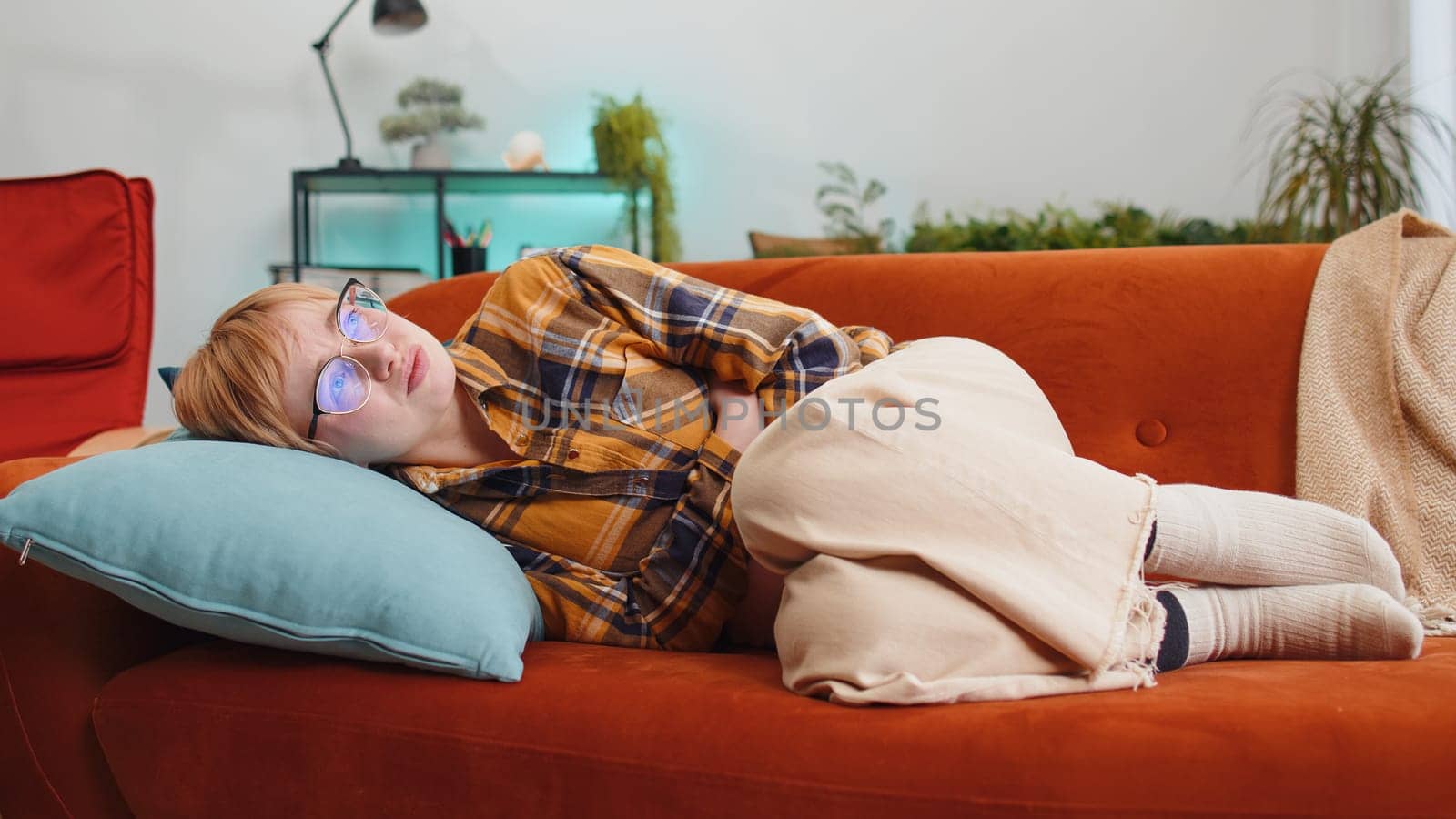 Sick ill woman suffering from painful stomach ache, period cramps lying on sofa at home room. Girl holding belly, feeling abdominal or menstrual pain. Abdominal pain, gastritis, diarrhea, indigestion