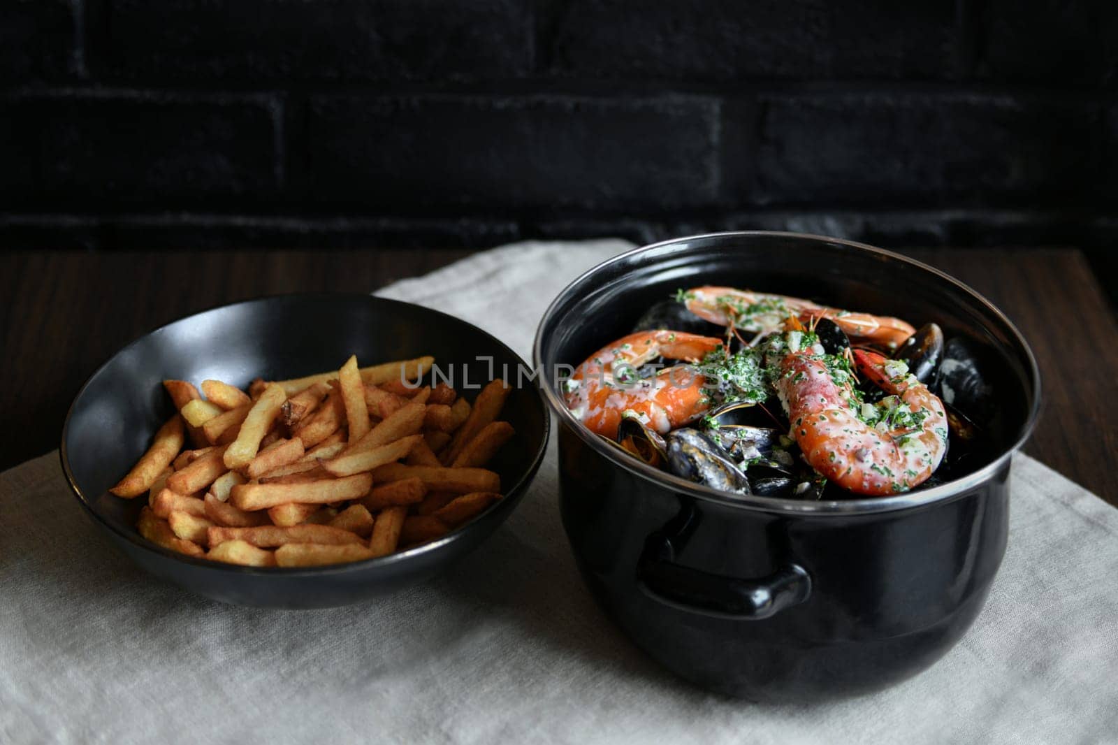 Mussels with sauce and shrimps and french fries on a black background