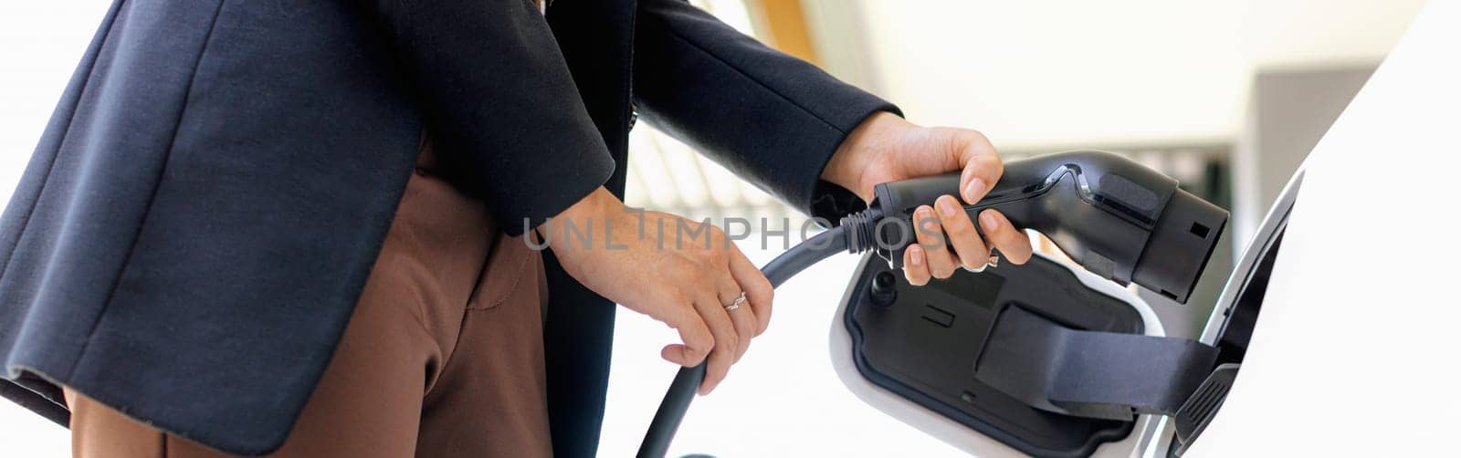 Closeup progressive woman install cable plug to her electric car with home charging station. Concept of the use of electric vehicles in a progressive lifestyle contributes to clean environment.