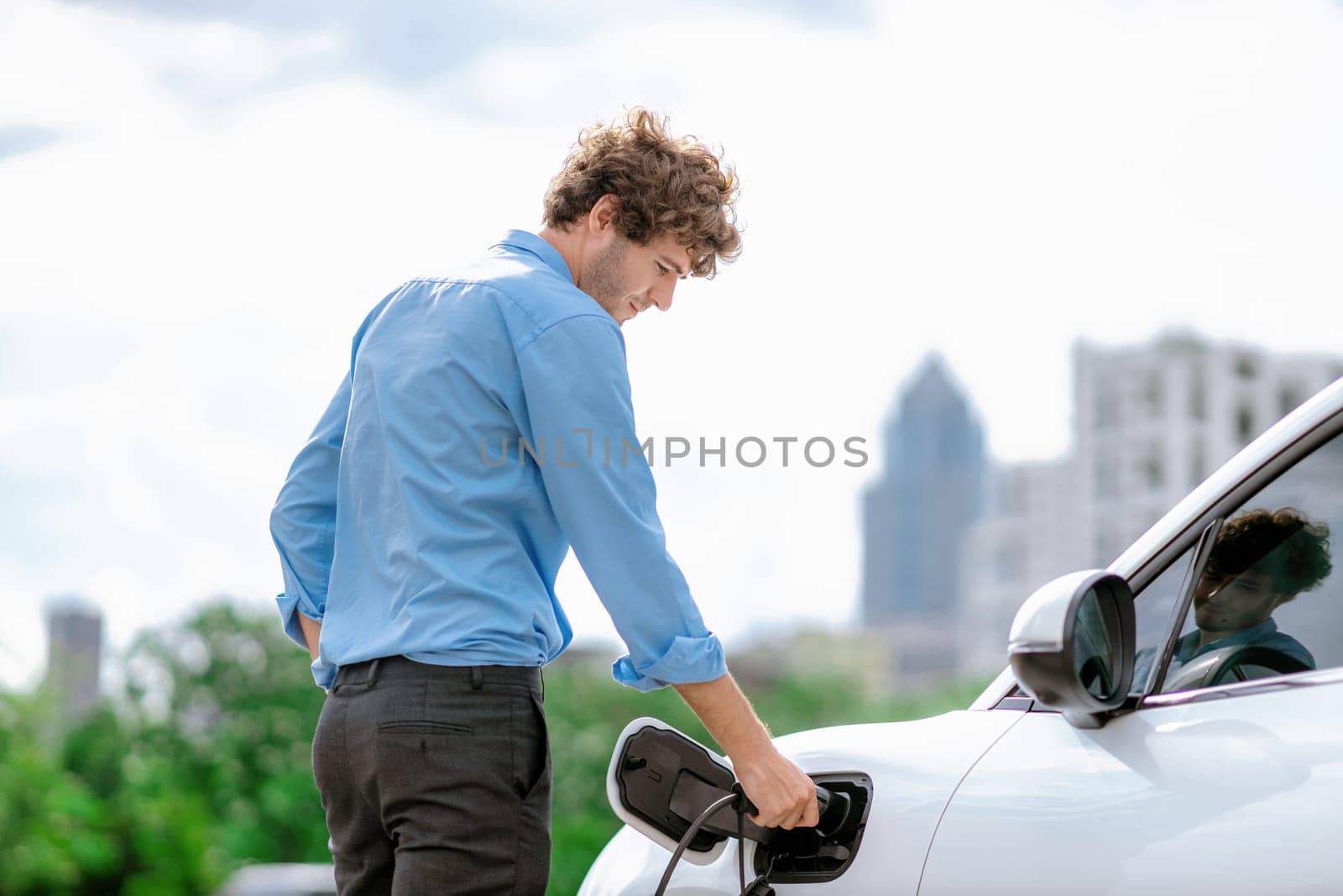 Progressive businessman plugs charger plug from charging station to EV. by biancoblue