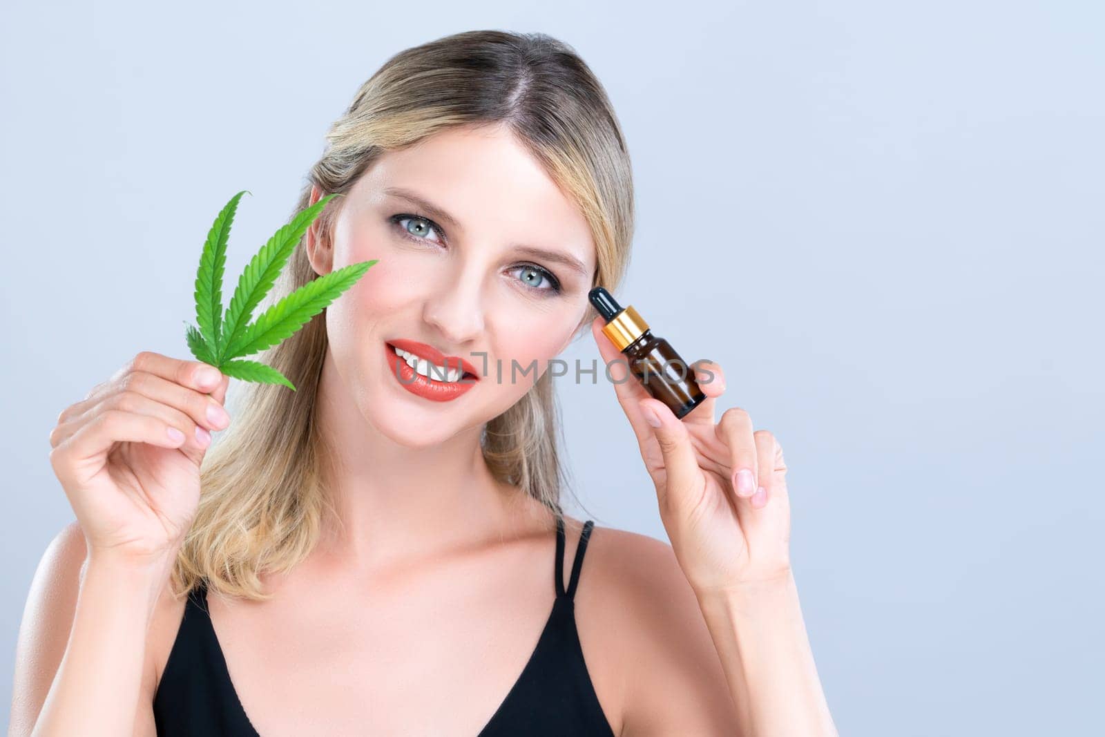 Alluring portrait of beautiful woman with perfect makeup hold green leaf, marijuan extracted bottle for skincare treatment product. Cannabis CBD oil for cosmetic and beauty in isolated background.