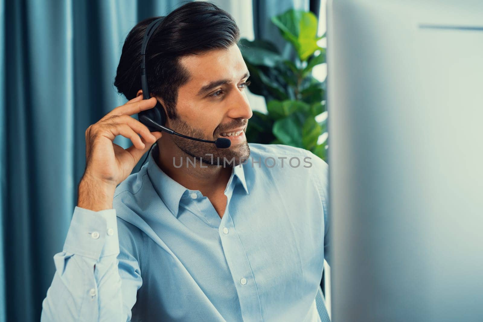 Male call center operator or telesales representative siting at his office desk wearing headset and engaged in conversation with client providing customer service support or making a sale. fervent