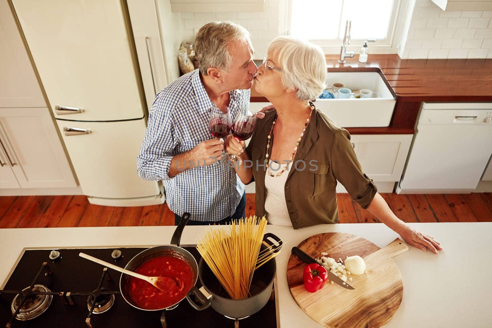 Kiss, wine toast or old couple cooking food for a healthy vegan diet together with love in retirement at home. Top view of senior woman drinking or kissing in kitchen with mature husband at dinner.