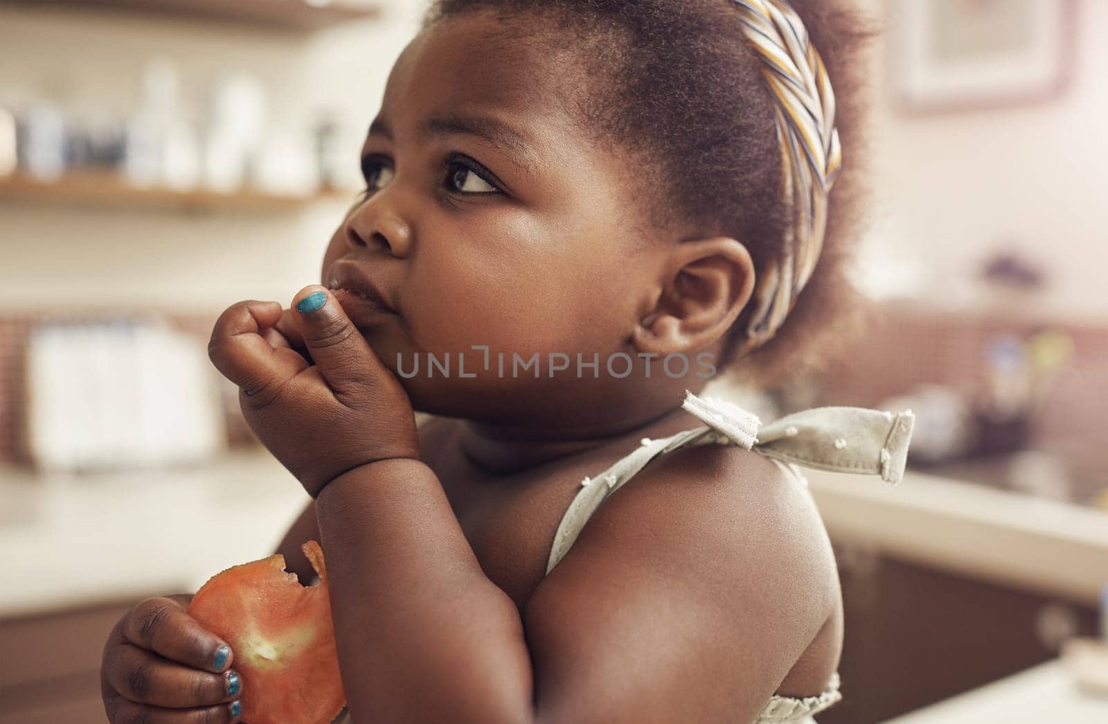 Black child, tomato and eating baby in a home kitchen with food and fruit at breakfast. African girl, nutrition and youth in a house with hungry kid feeling relax with natural, healthy snack for kids.