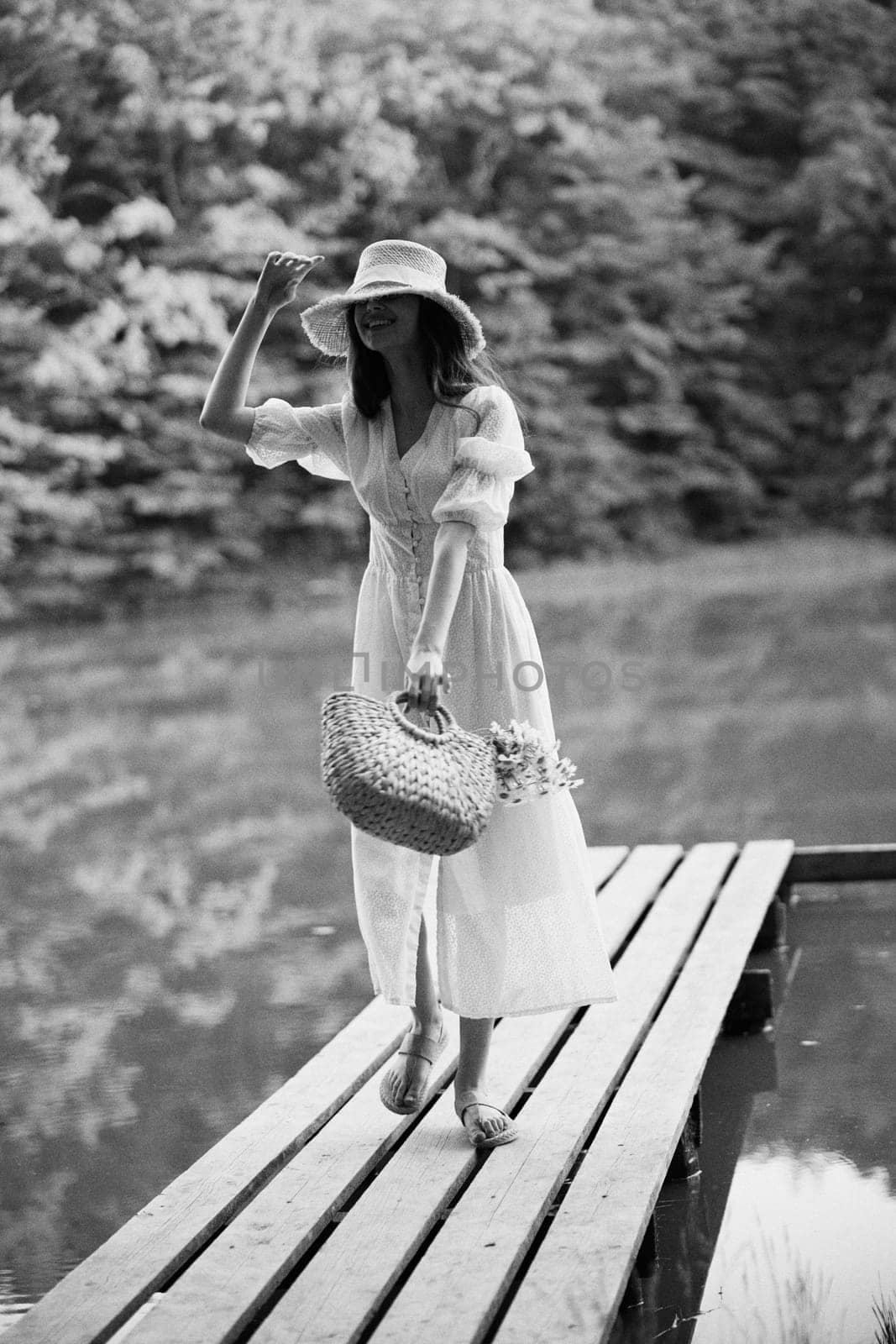 monochrome photo of a woman on the pier of a forest lake with a wicker hat looking at the camera. High quality photo