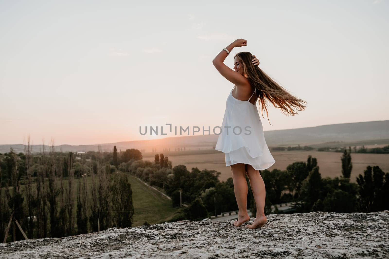 Romantic beautiful bride in white dress posing with sea and mountains in background. Stylish bride standing back on beautiful landscape of sea and mountains on sunset