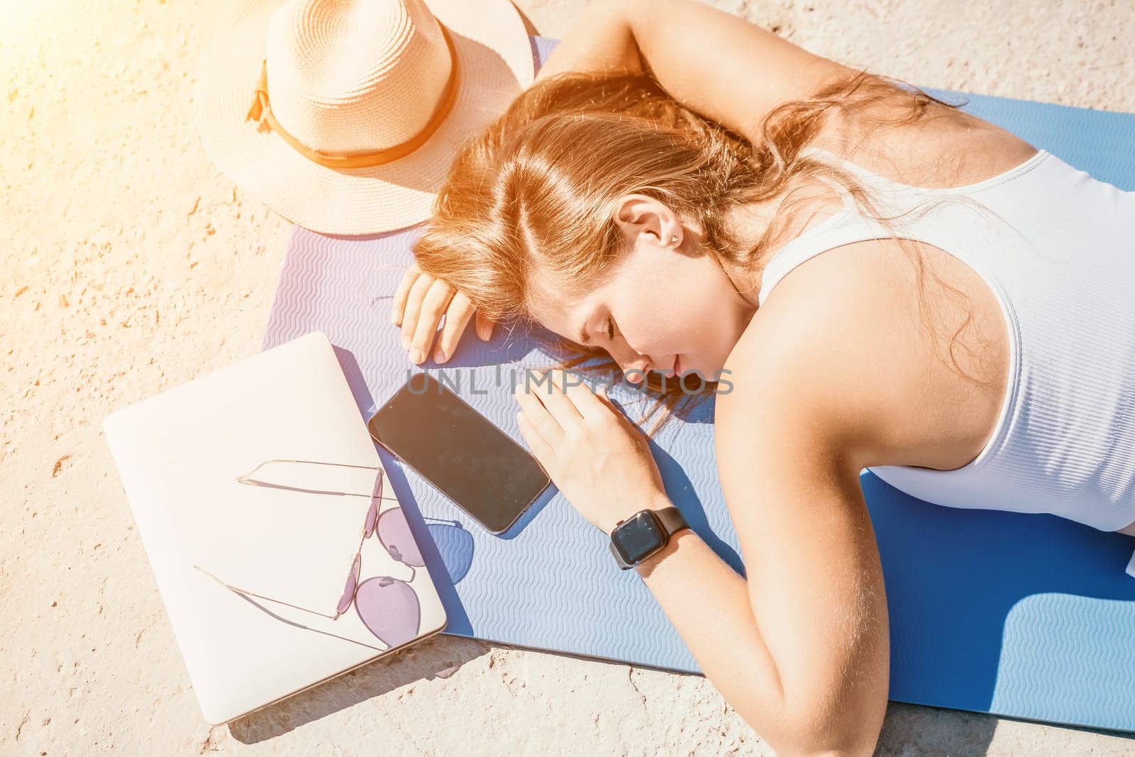 Successful business woman in yellow hat working on laptop by the sea. Pretty lady typing on computer at summer day outdoors. Freelance, travel and holidays concept.