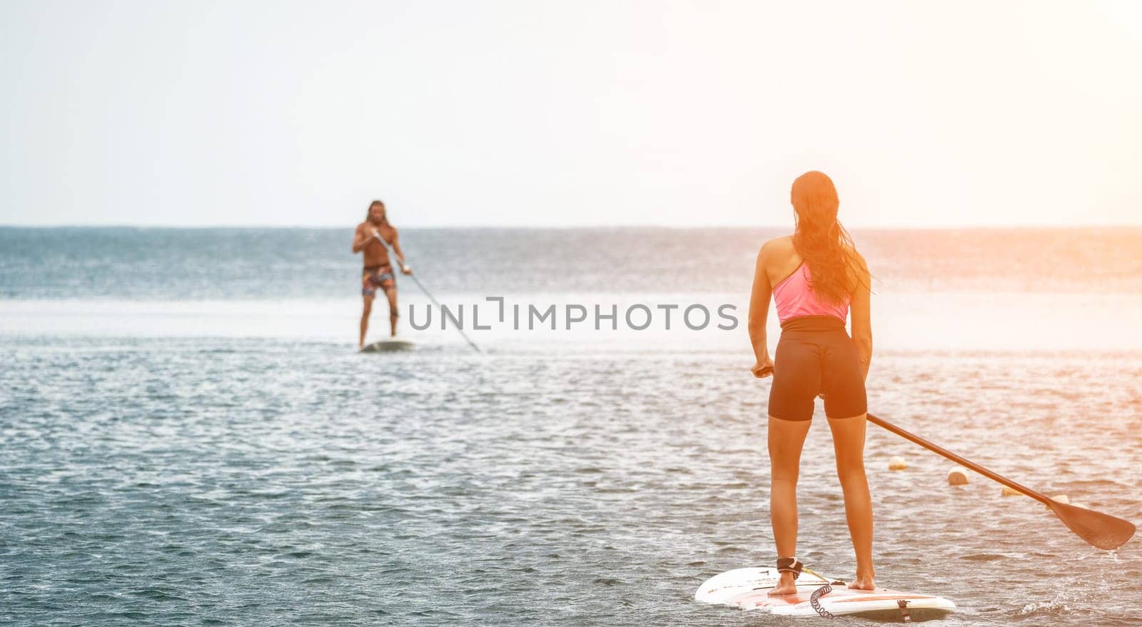 Sea woman and man on sup. Silhouette of happy young woman and man, surfing on SUP board, confident paddling through water surface. Idyllic sunset. Active lifestyle at sea or river