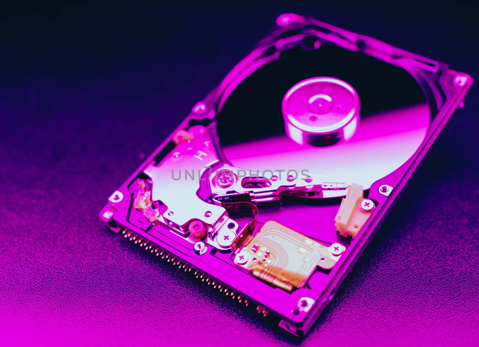 An open hard disk disassembled HDD of a computer or laptop lies on a purple surface. Computer hardware and accessories. Hard disk storage. by Unimages2527