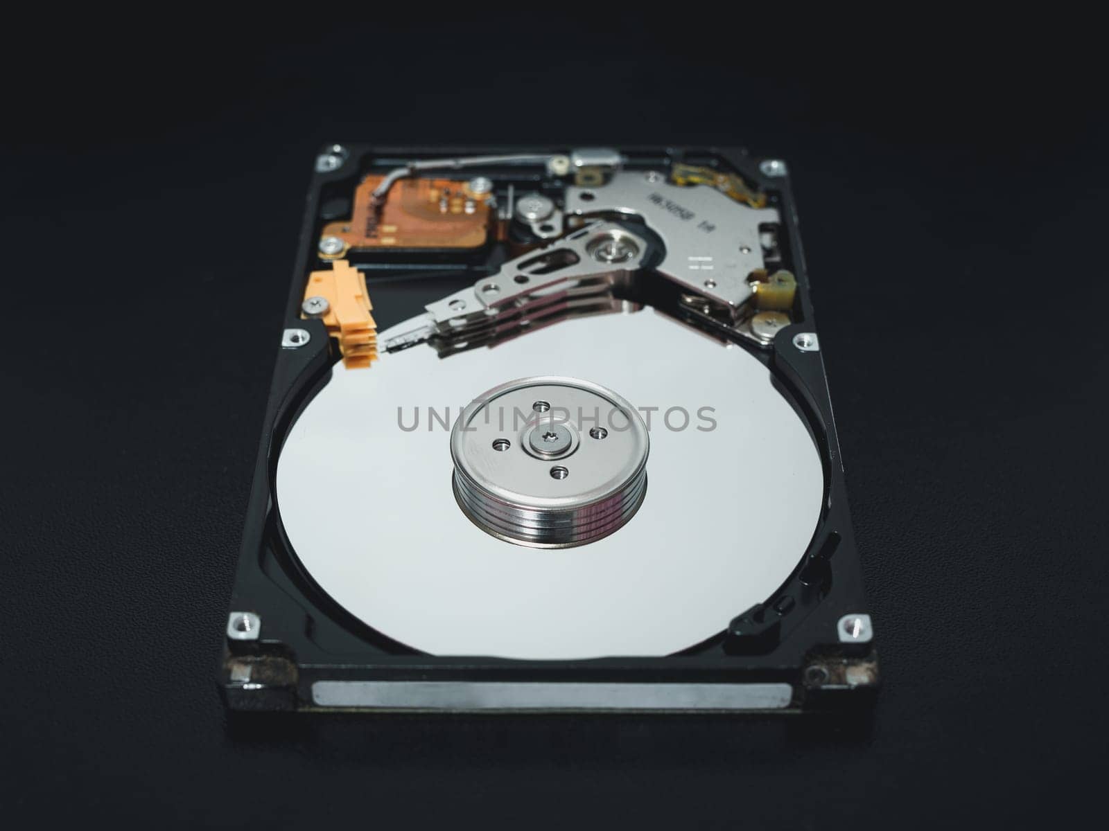 Disassembled open hard disk drive HDD of computer or laptop lies on dark matte surface. Сomputer hardware and equipment. Harddisk data storage. by Unimages2527