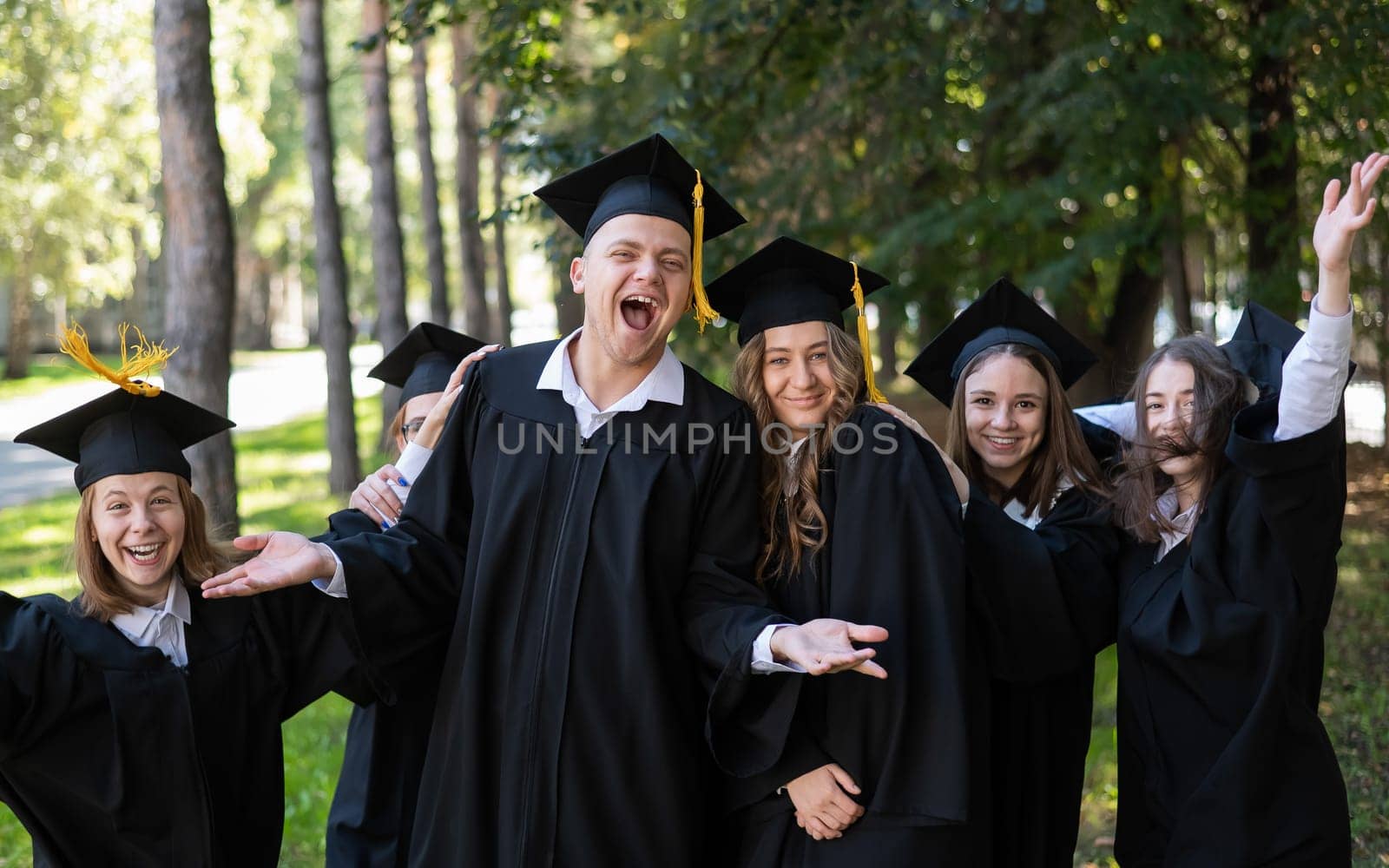 A group of graduates in robes congratulate each other on their graduation outdoors