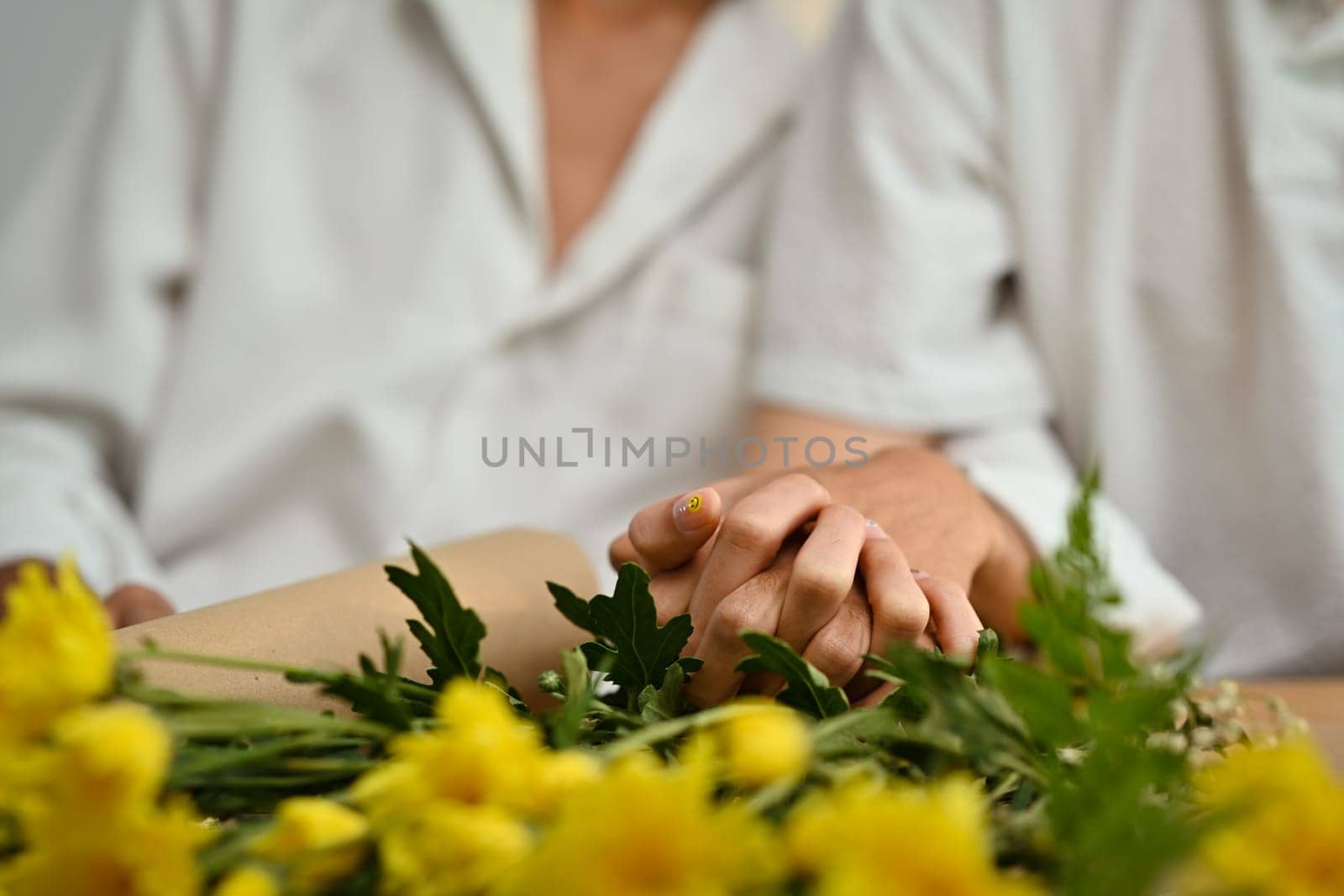 Anonymous gay couple clasping hands as symbol of homosexual love on table with flowers. LGBT, love and human rights concept.