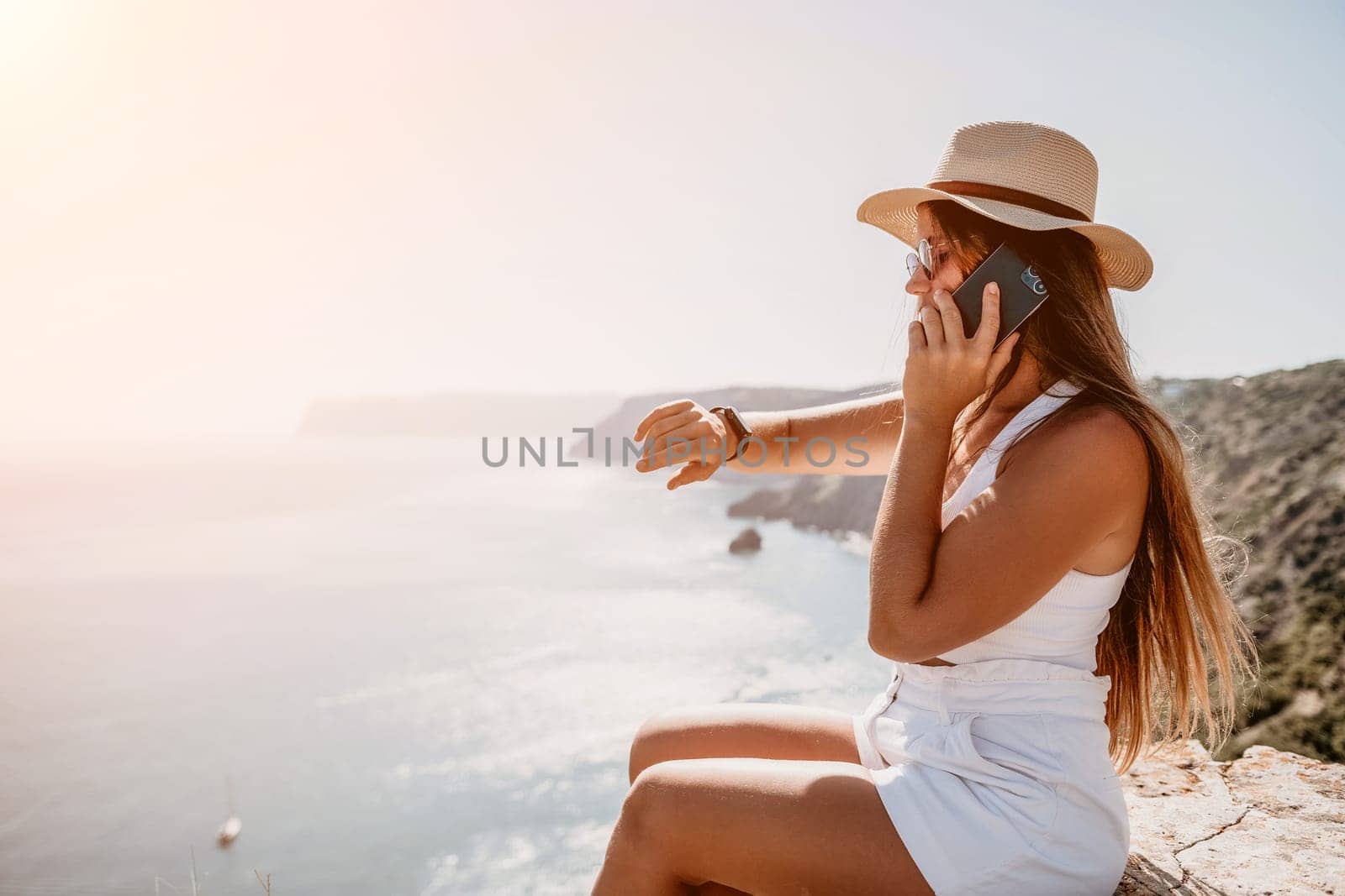 Successful business woman in yellow hat working on laptop by the sea. Pretty lady typing on computer at summer day outdoors. Freelance, travel and holidays concept.