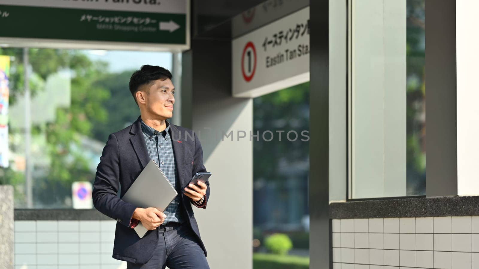 Businessman in full suit using smartphone in subway station during his morning commute.