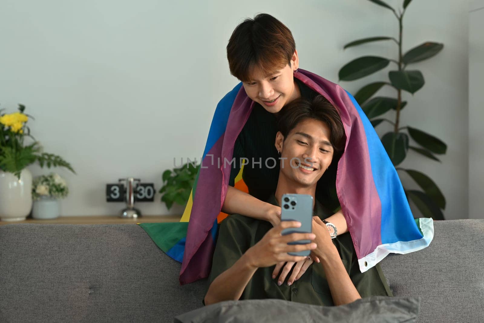 Cheerful two men couple using smartphone, relaxing on couch at home. LGBT, love and lifestyle relationship concept.