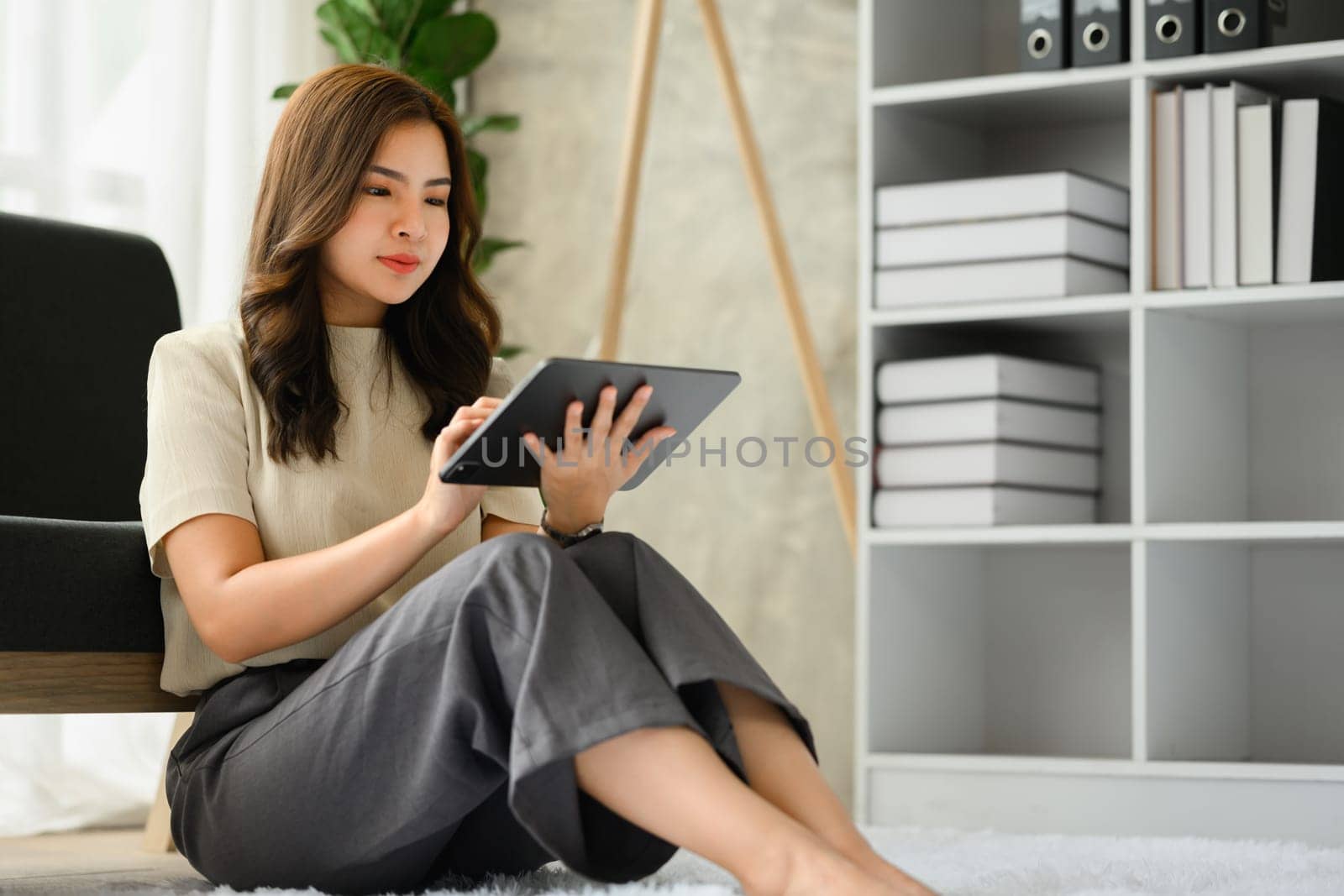 Casual millennial asian woman sitting on floor in living room and using digital tablet. Technology, people and lifestyle concept.