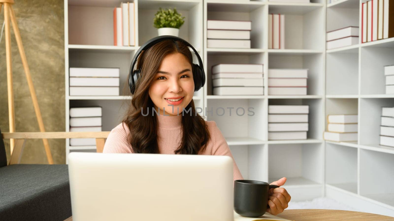 Attractive millennial woman in headphone communicating online or distantly working on laptop at home.