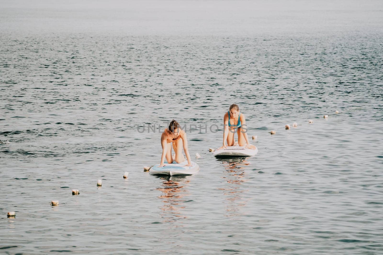 Woman sup yoga. Middle age sporty woman practising yoga pilates on paddle sup surfboard. Female stretching doing workout on sea water. Modern individual hipster outdoor summer sport activity