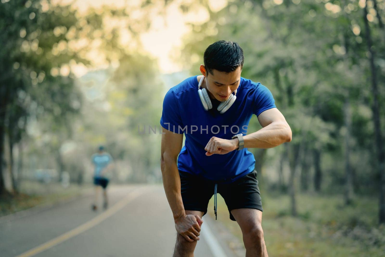 Portrait of tired male runner checking pulse or training results on smartwatch. Technology health, wellness concept.