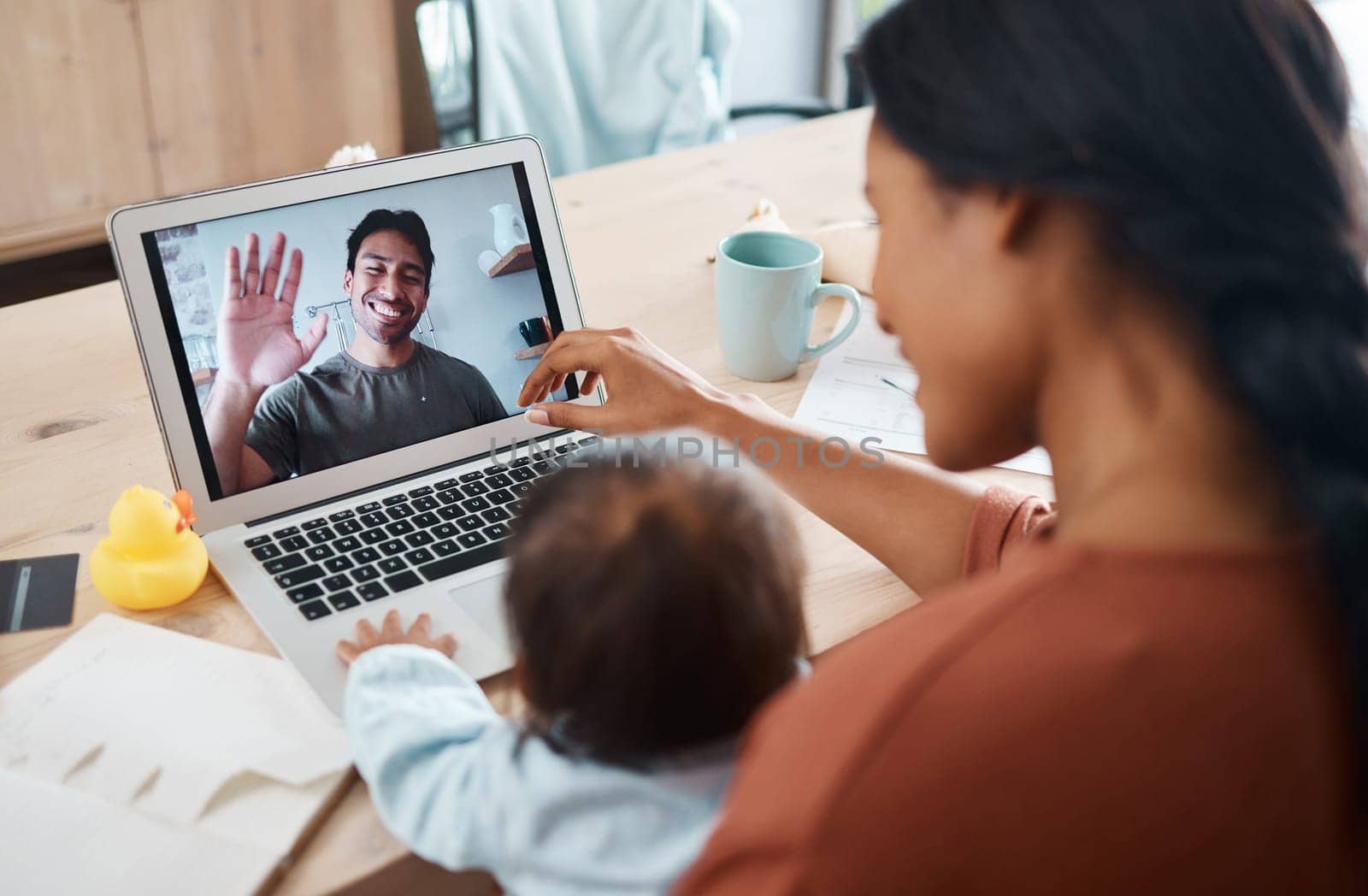 Family on video call, mom and baby happy to see smiling father waving with laptop webcam to talk to each other. Mother, young child talking to dad at work from home and using 5g streaming technology.