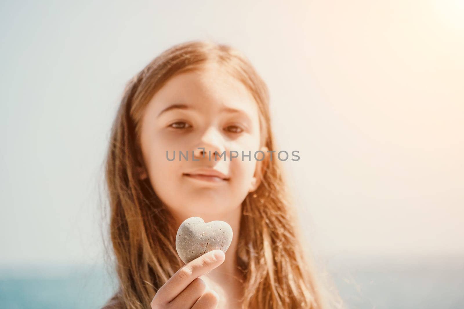Happy girl holding in hand a stone in the shape of a heart against the background of the sea. Summer holiday vacation and travel concept. by panophotograph