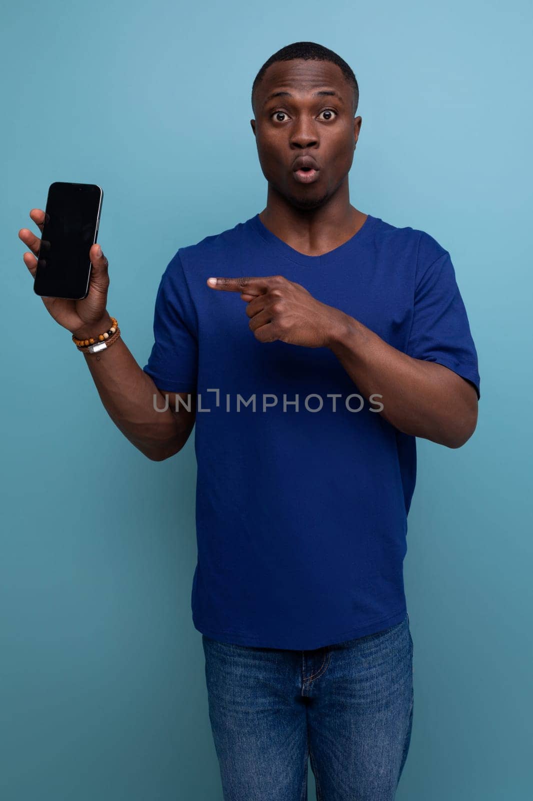 handsome young american man in blue t-shirt holding phone with screen mockup.