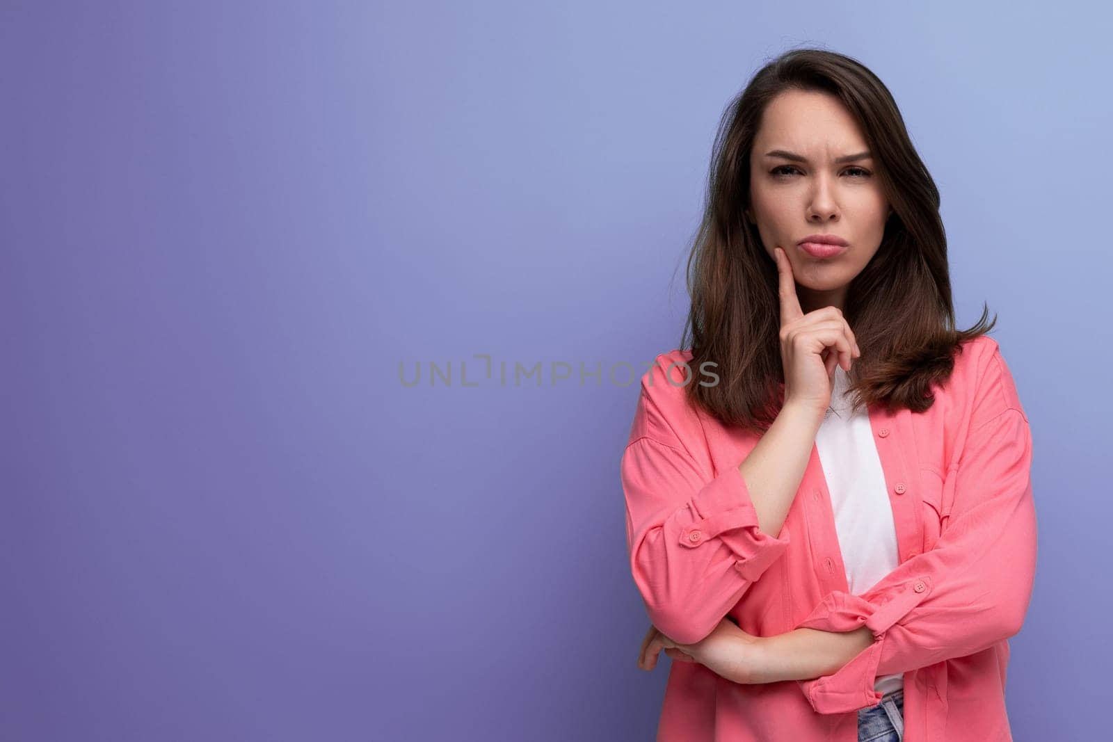 portrait of a well-groomed european young black-haired woman with shoulder-length hair in a pink shirt on a studio background with copy space.