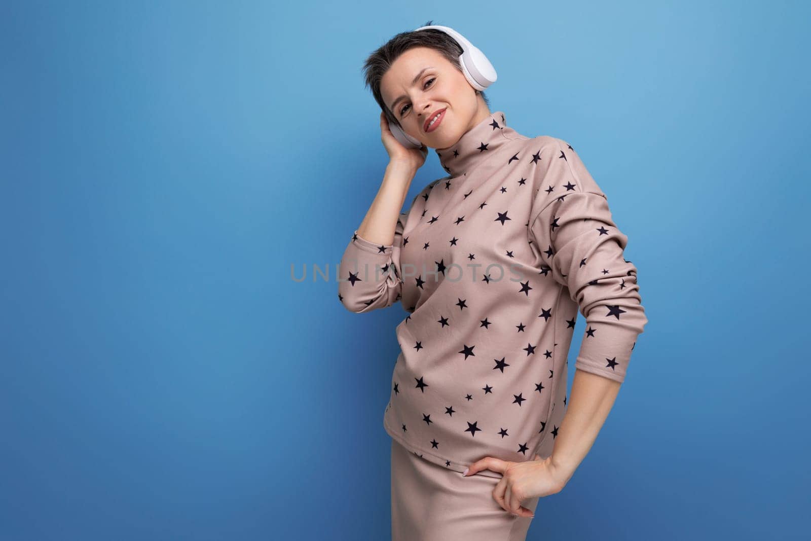 active bright caucasian young woman with a short haircut dressed in a beige suit listens to music in wireless bluetooth headphones.