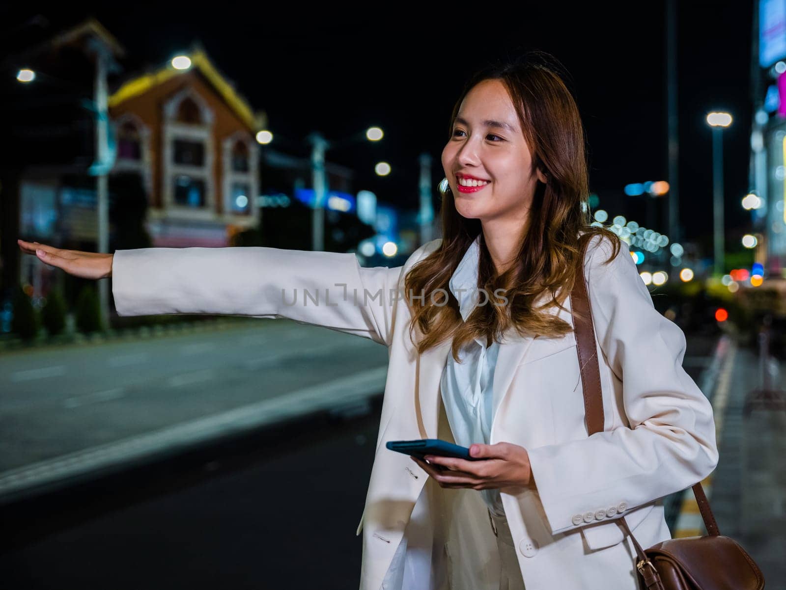 businesswoman standing hail waving hand taxi on road in busy city street at night by Sorapop