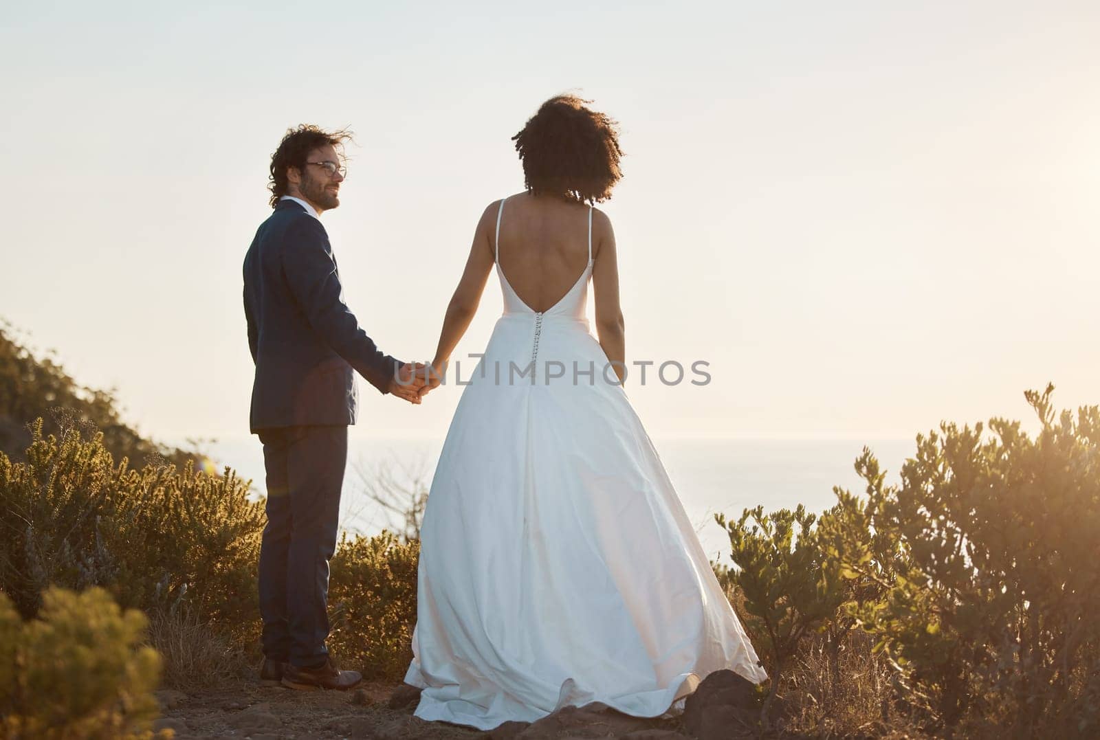 Love, wedding and holding hands with couple in nature park for celebration, romance and happiness. Sunset, support and summer with bride and groom in countryside for marriage, ceremony and bonding by YuriArcurs