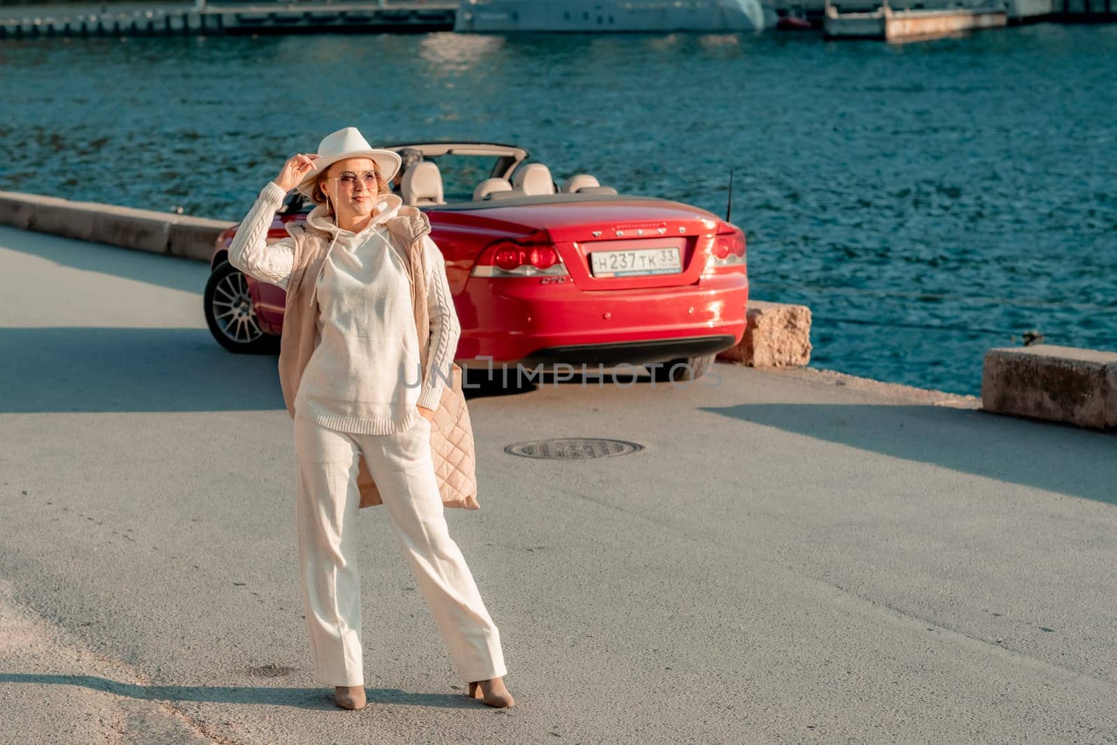 Portrait of a blonde convertible. Fashionable attractive woman with blond hair in a white hat on the background of a red car and the sea