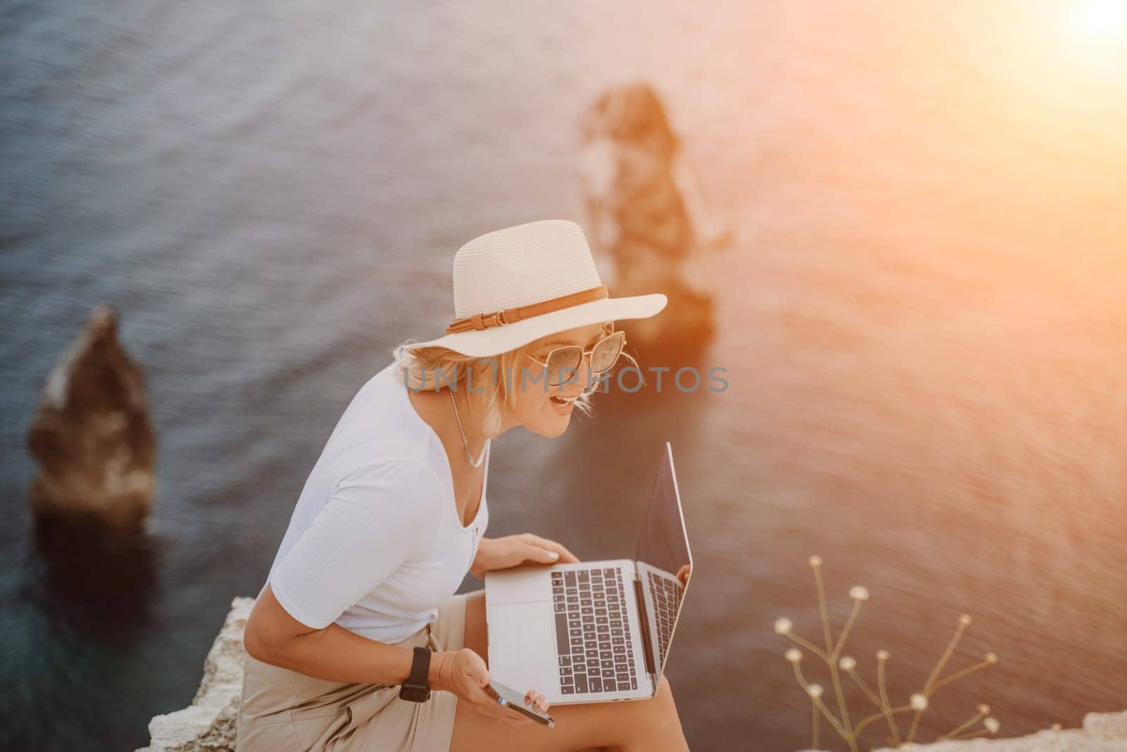 Freelance women sea working on the computer. Good looking middle aged woman typing on a laptop keyboard outdoors with a beautiful sea view. The concept of remote work
