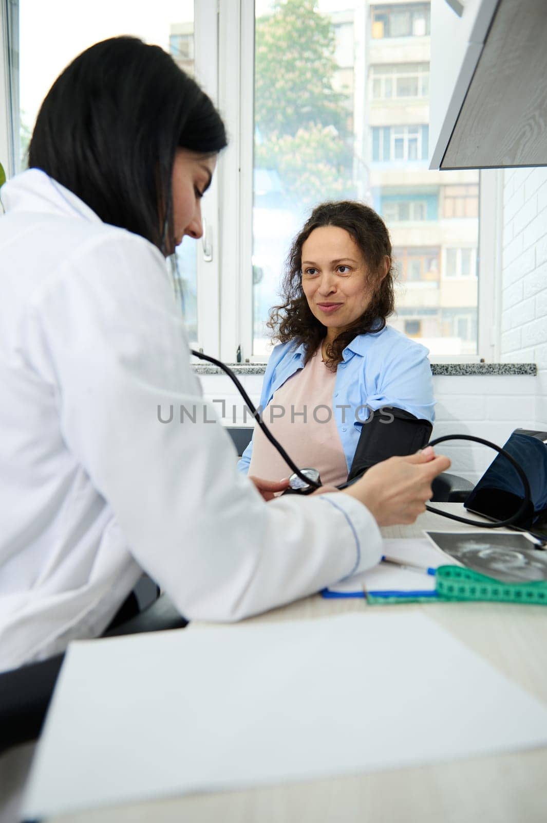 Happy pregnant woman at appointment with female doctor, obstetrician gynecologist. GP taking blood pressure in office by artgf