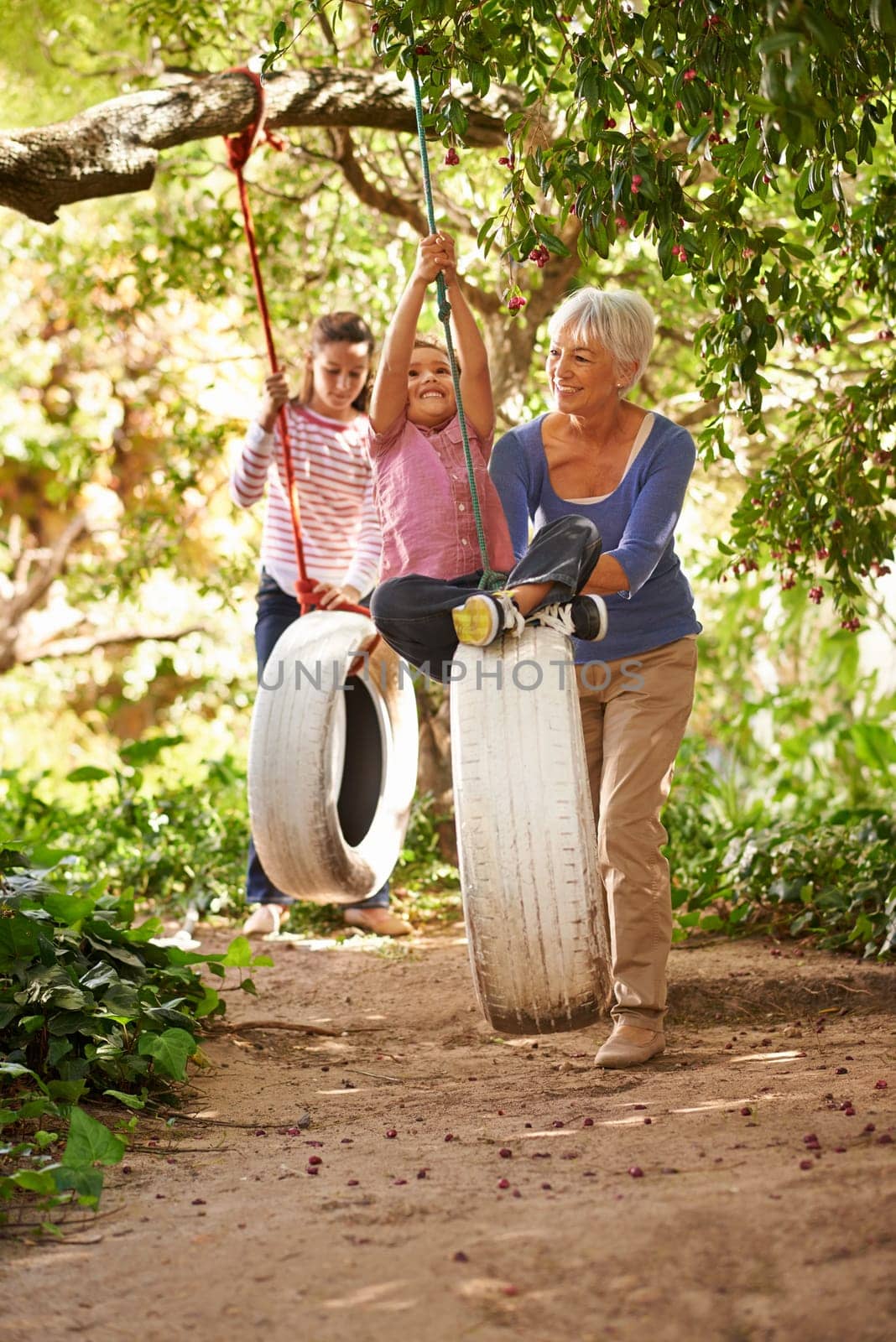 Elderly woman, tire swing and grandma playing with grandkids or holidays and having fun in a garden in summer. Excited, grandchildren and outdoors swinging together or on sunny weekend at a park.