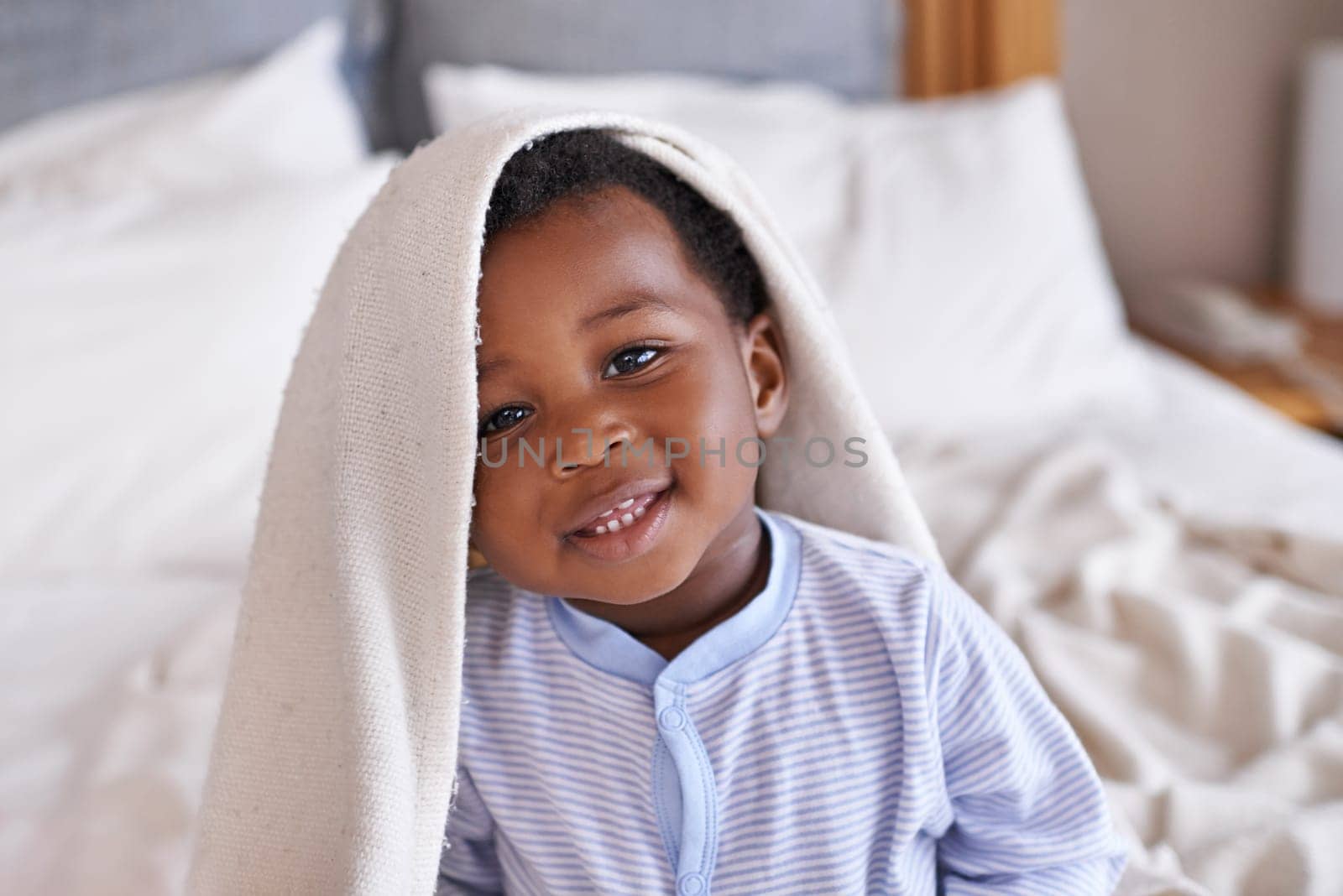 Portrait, happy and baby with a blanket in bed, waking up and playing in his home. Face, smile and african boy toddler in a bedroom curious, having fun and sweet, cute and playful while relaxing.