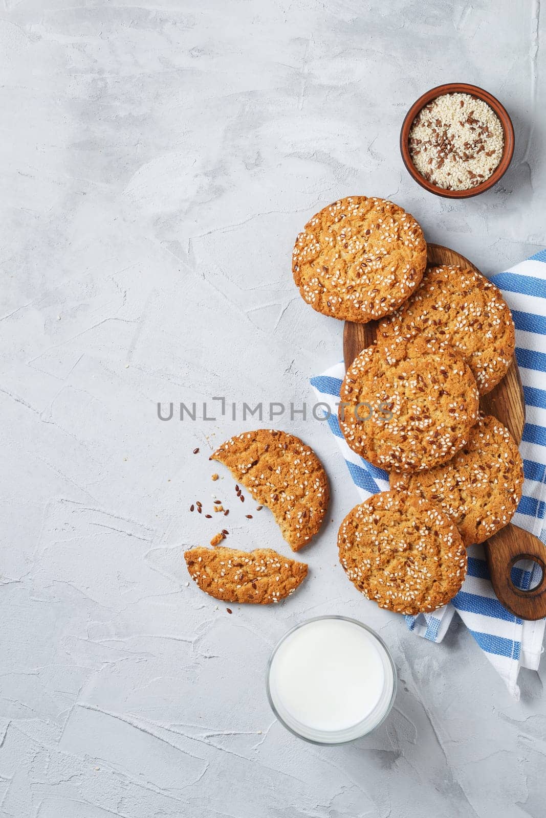 Oatmeal cookies with sesame seeds and flax seeds on a gray background with a jar of oatmeal and a glass of milk.Copy space