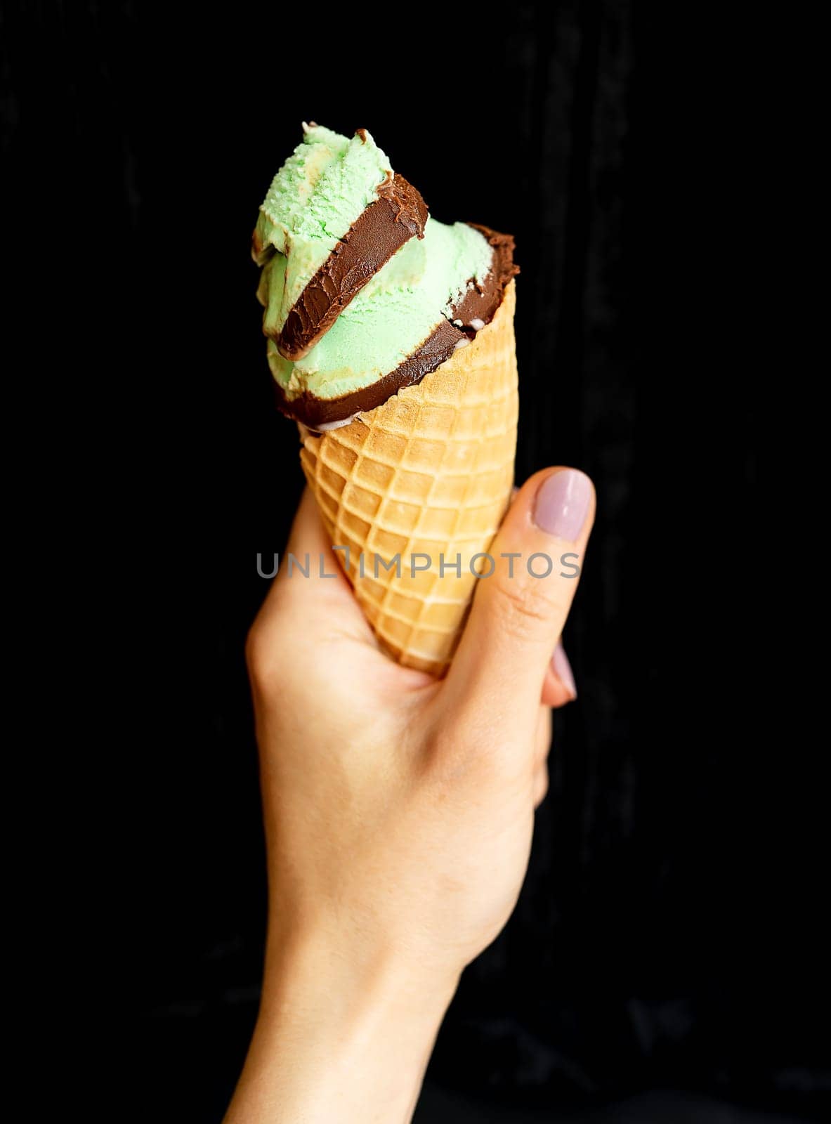 The hand holds soft ice cream in a chocolate-mint waffle cup. On a black background, close-up