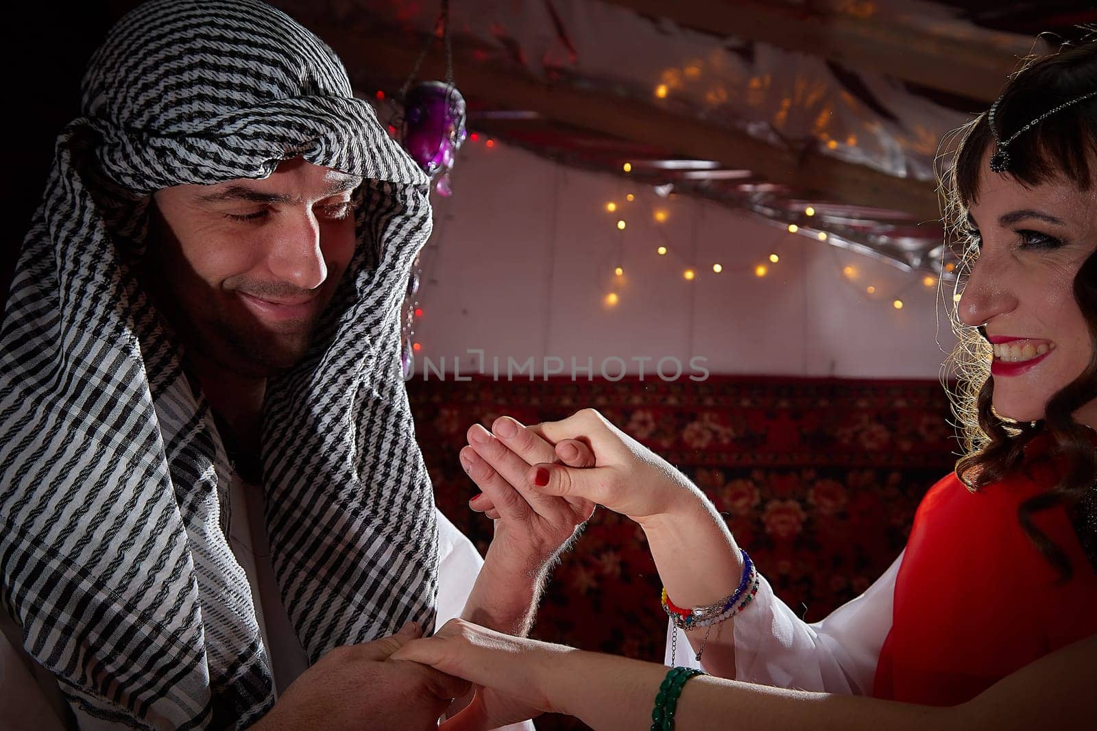 Portrait of young arabian muslim couple in traditional clothes in cozy red room. Fhoto shoot in easten style with male and female model like in a harem with a sultan and an odalisque. Partial focus by keleny