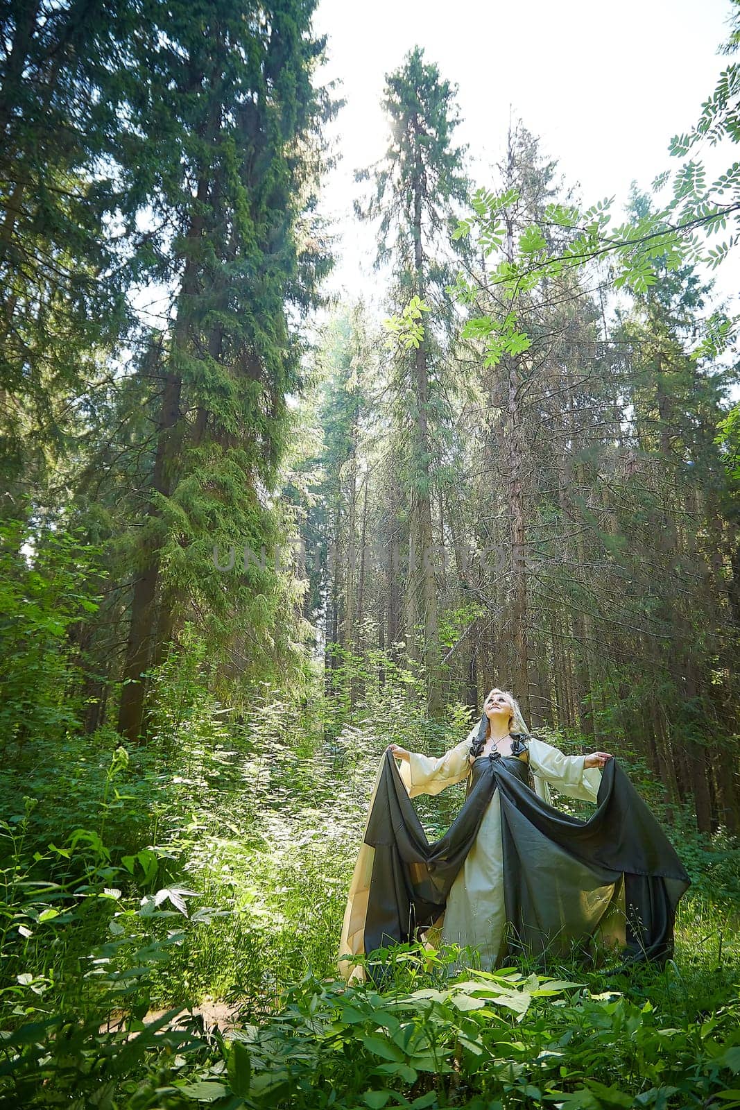 Adult mature woman 40-60 in a green long fairy dress in forest. Photo shoot in style of dryad and queen of nature. Fairy who loves nature in beautiful green summer forest. Concept of caring for nature by keleny