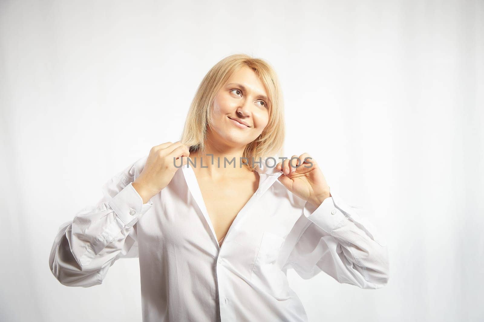 Portrait of a pretty blonde smiling woman posing on a white background. Happy girl model in white shirt posing in studio. Copy space by keleny