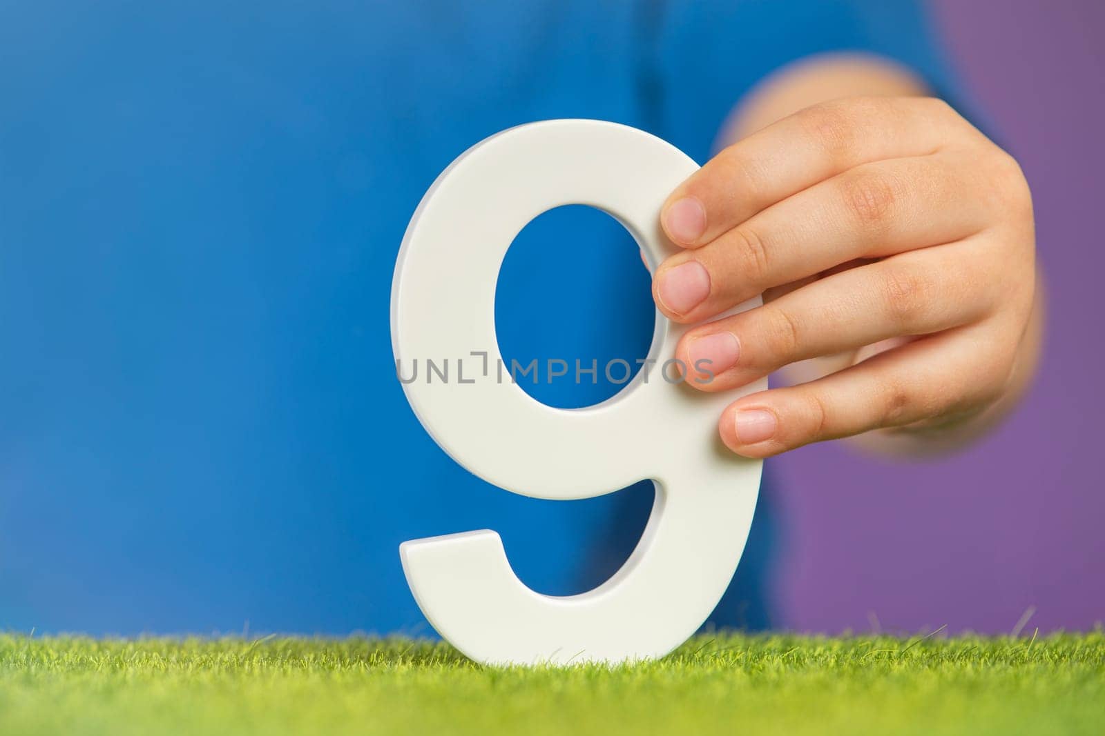 Number 9 in hand. A hand holds a white number nine on a purple background, nine percent per annum. Advertising banner or greeting card. Concept for Europe Day, May 9th. High quality photo