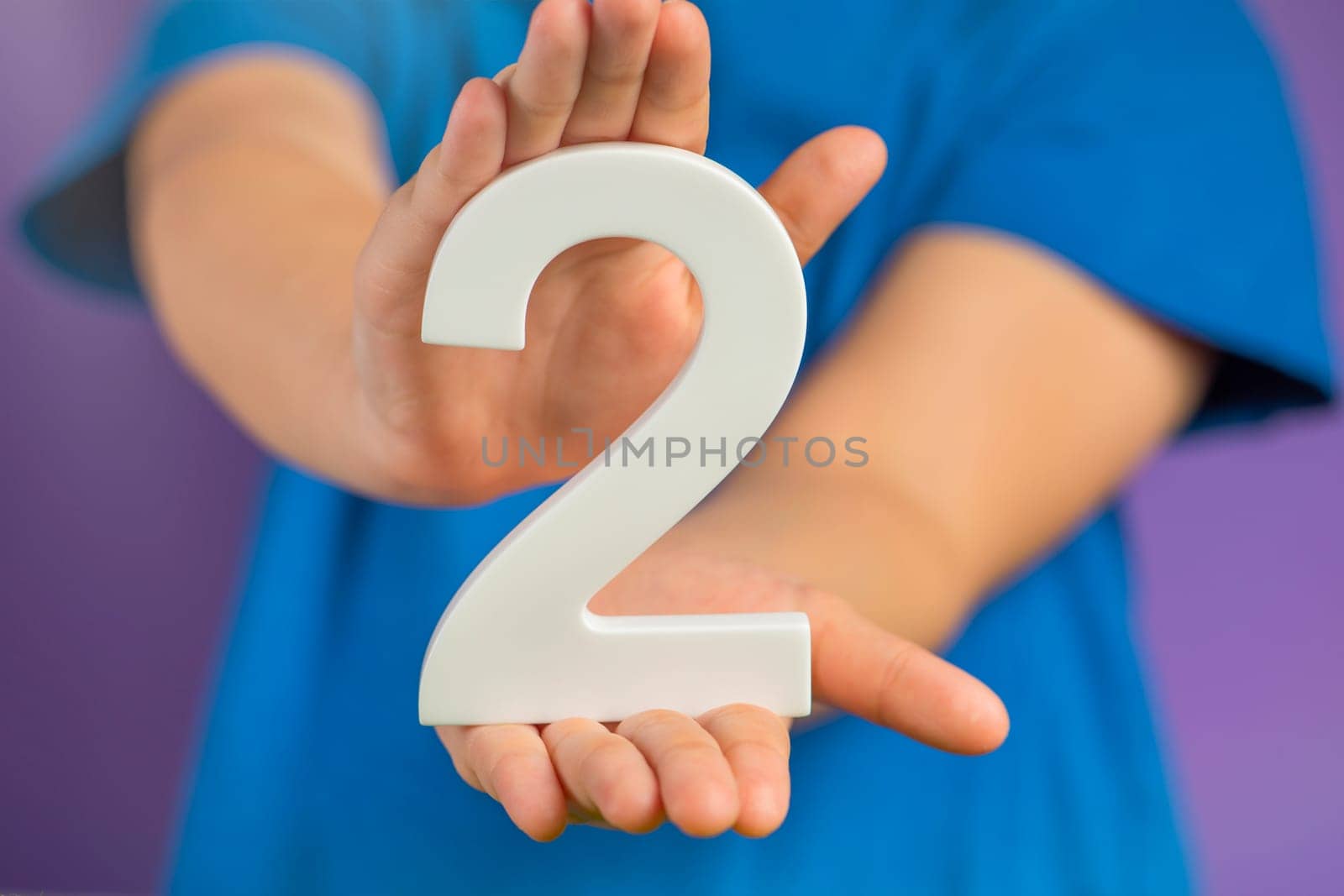 White number 2 in hand. The hand holding the number 2 symbolizes choice, partnership and duality, the choice between two alternatives, to combine the efforts of two people to achieve a common goal