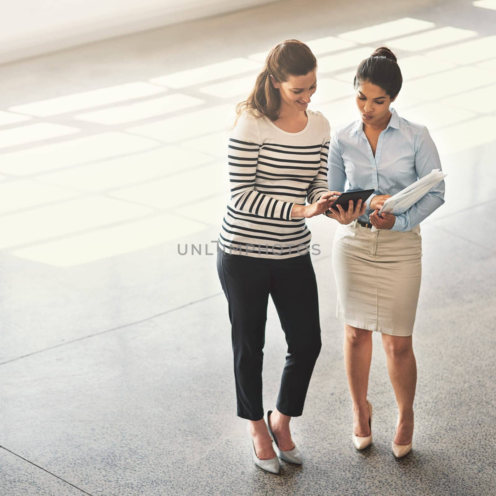Comparing digital and analog ideas. High angle shot of two businesswomen talking together while standing in an office lobby