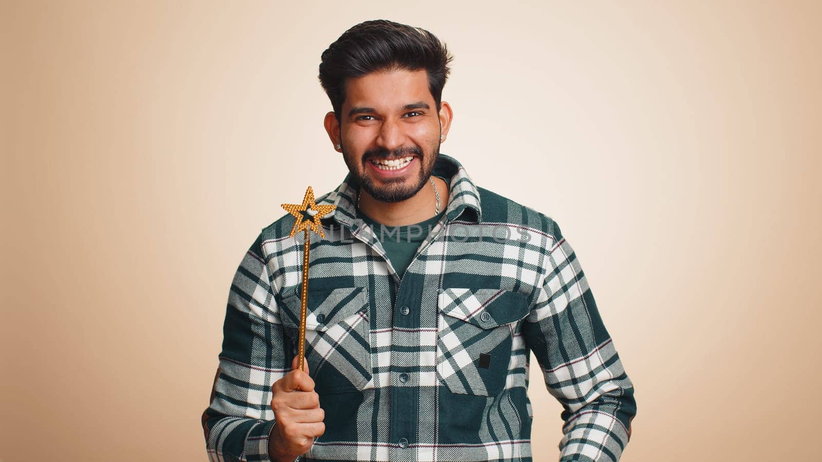 Magician wizard man gesturing with magic wand fairy stick, making wish come true, casting magician spell, advertising holidays sale discount. Handsome indian guy isolated on beige studio background
