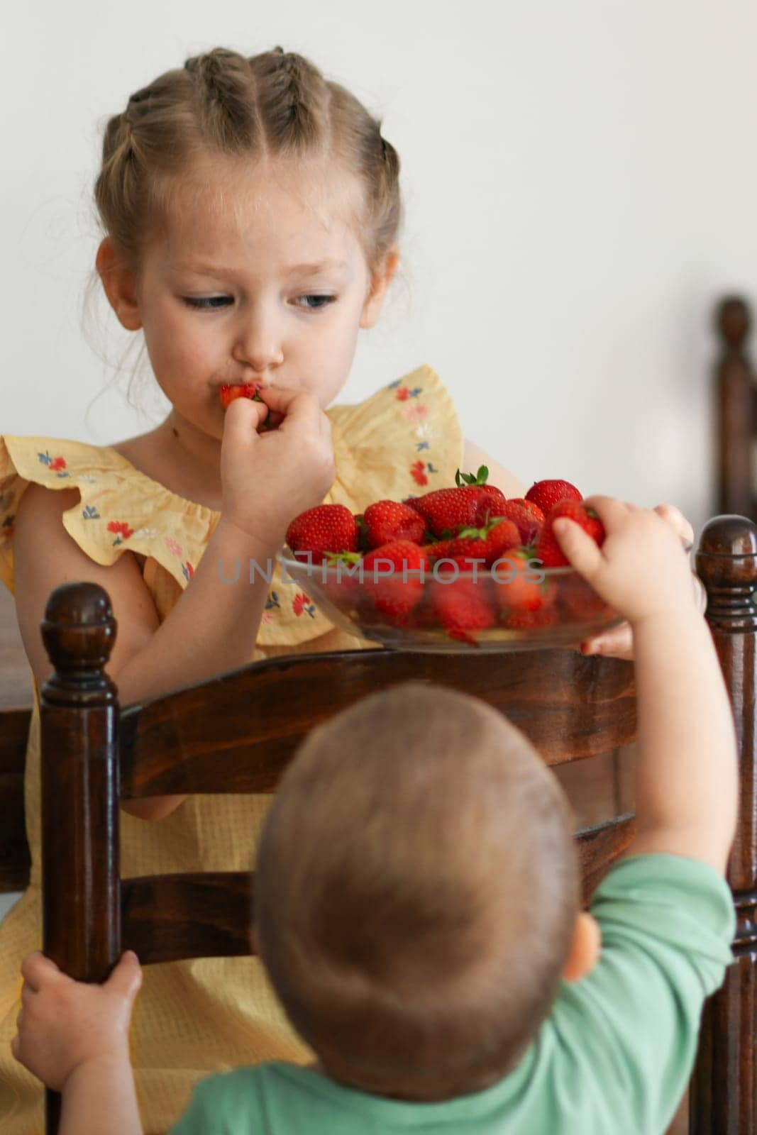 Two young girls eating strawberries in living room smiling