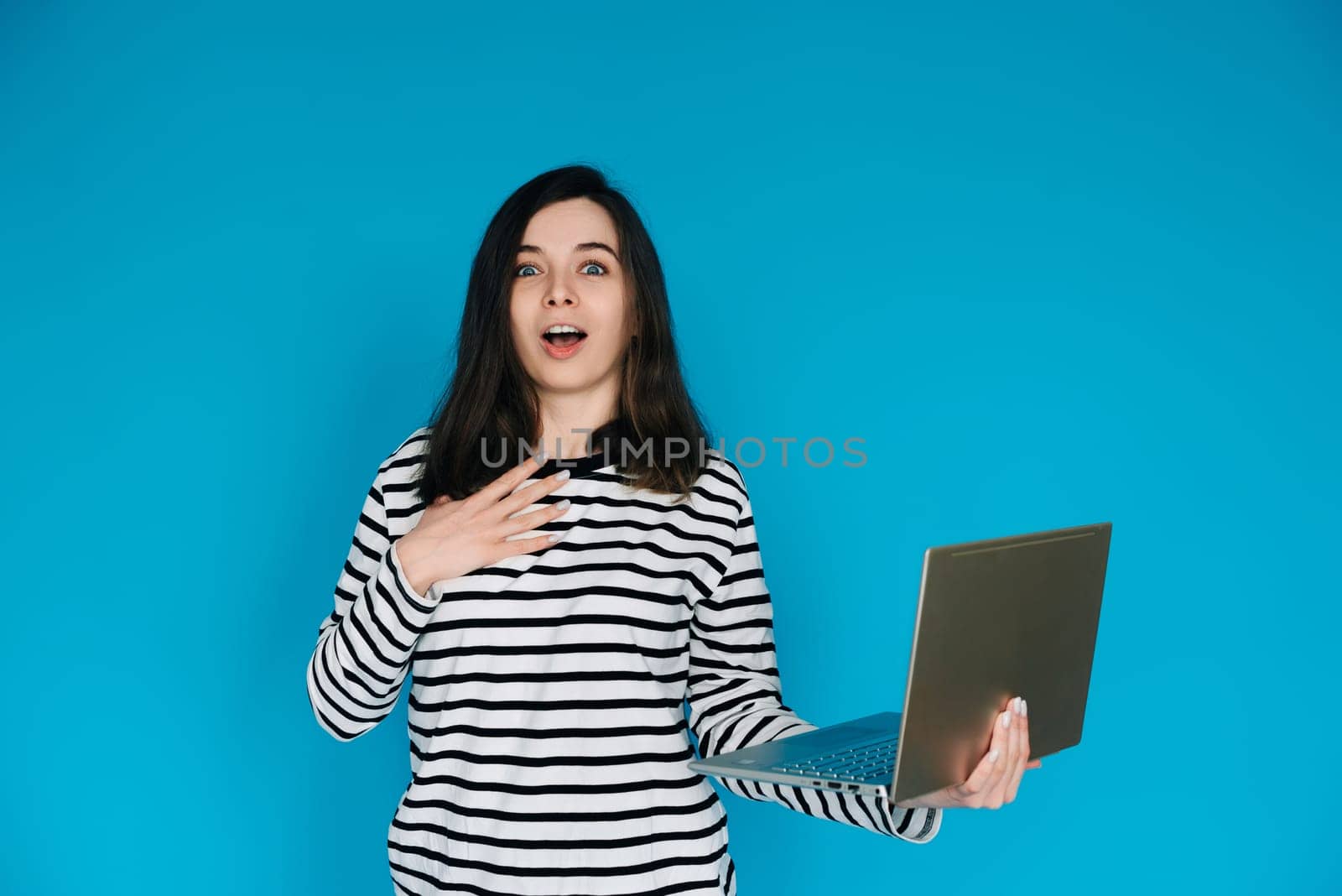 Excited Woman in Striped Sweater Writing Email on Laptop - Modern Technology and Communication Concept. Empty Space for Text - Isolated on Blue Background - Perfect for Business and Technology Themes