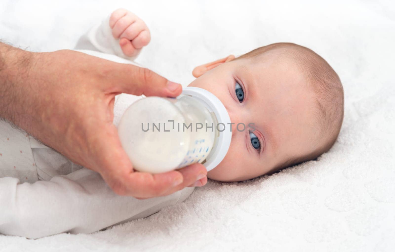 Baby eats formula from a bottle supported by his father.