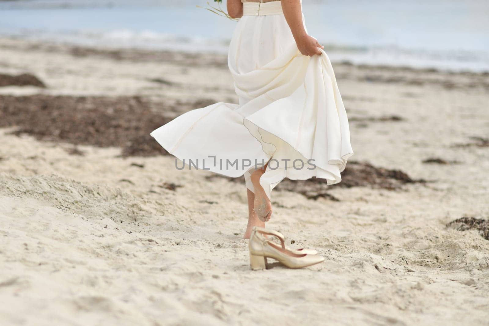 Bride in white dress and golden shoes on the sandy beach
