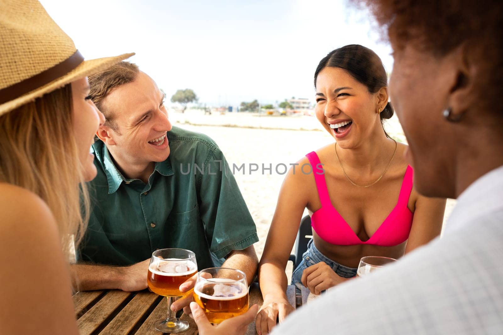 Young hispanic woman laughing and enjoying vacation with friends. Multiracial people having beer together at a beach bar. Lifestyle concept.